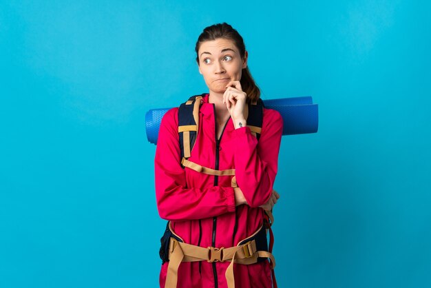 Young mountaineer woman over isolated blue wall having doubts and thinking