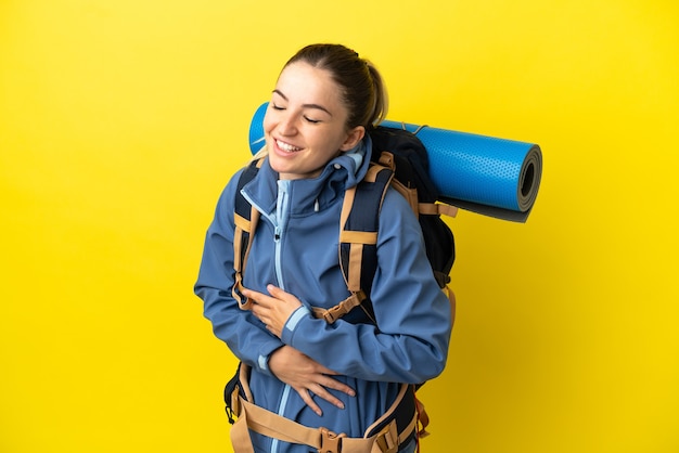 写真 たくさん笑って孤立した黄色の背景の上に大きなバックパックを持つ若い登山家の女性