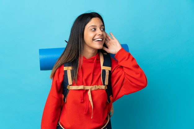 Young mountaineer woman with backpack listening to something by putting hand on the ear