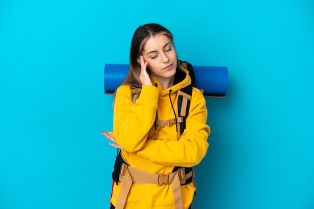 Young mountaineer woman with a big backpack isolated on blue wall with headache