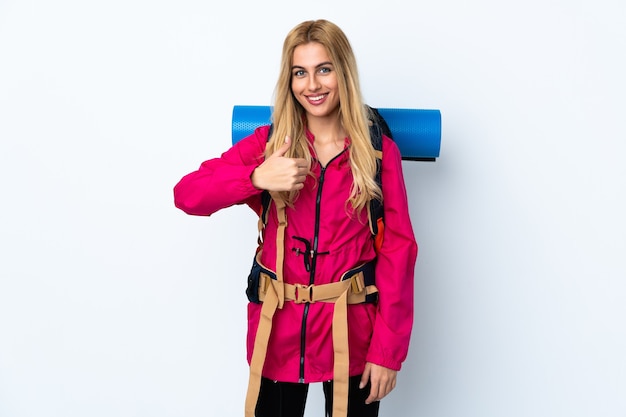 Young mountaineer woman with a big backpack isolated giving a thumbs up gesture