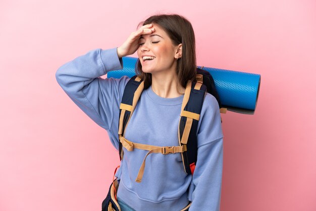 Young mountaineer woman with a big backpack isolated on pink background smiling a lot