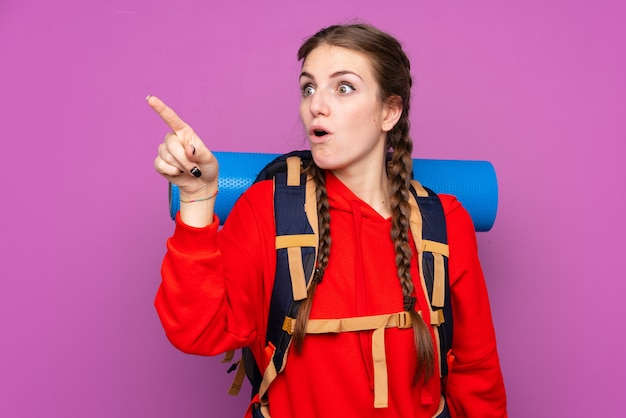 Young mountaineer woman with a big backpack over isolated wall