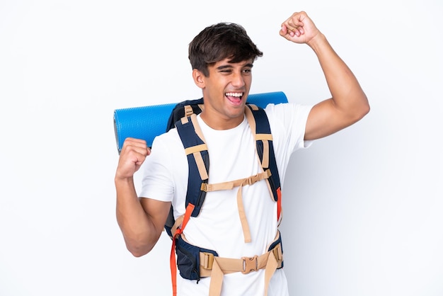 Young mountaineer woman with a big backpack over isolated white background celebrating a victory