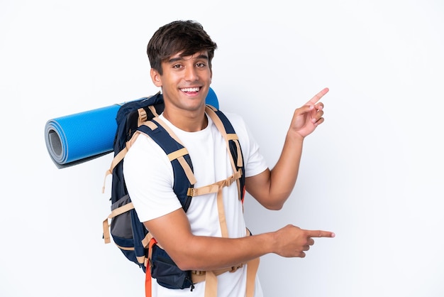 Young mountaineer woman with a big backpack over isolated white background pointing finger to the side and presenting a product