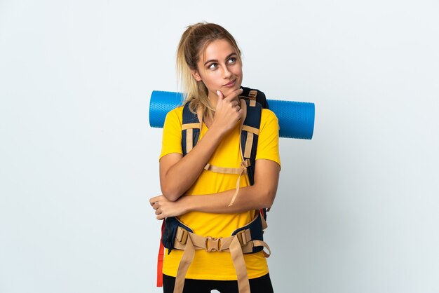 Young mountaineer woman with a big backpack isolated on white space having doubts and thinking