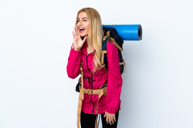 Young mountaineer woman with a big backpack over isolated white space shouting with mouth wide open