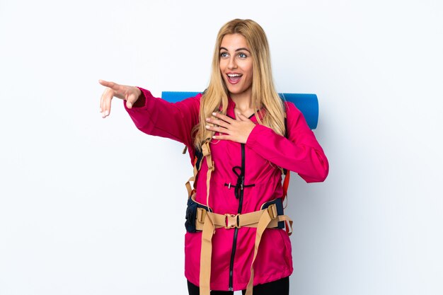 Young mountaineer woman with a big backpack over isolated white wall pointing finger to the side