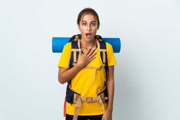 Young mountaineer woman with a big backpack isolated on white wall surprised and shocked while looking right