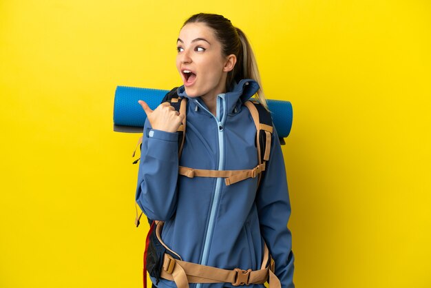 Young mountaineer woman with a big backpack over isolated yellow background intending to realizes the solution while lifting a finger up