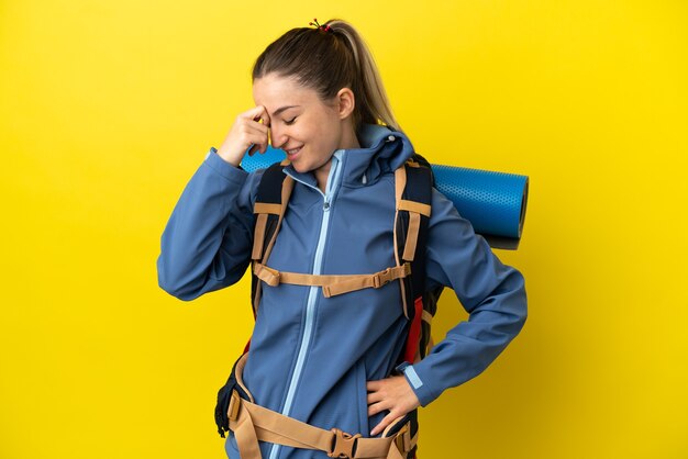 Young mountaineer woman with a big backpack over isolated yellow background laughing