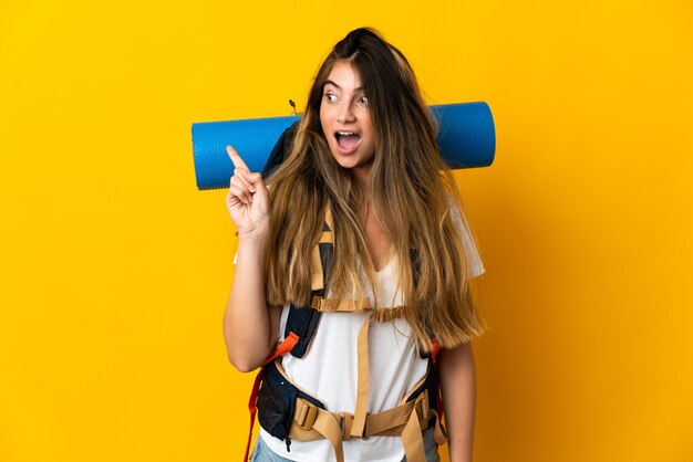 Young mountaineer woman with a big backpack isolated on yellow wall intending to realizes the solution while lifting a finger up