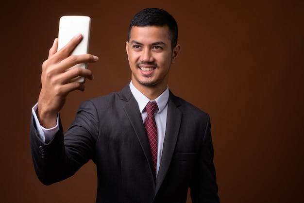 Young multi-ethnic Asian businessman against brown wall