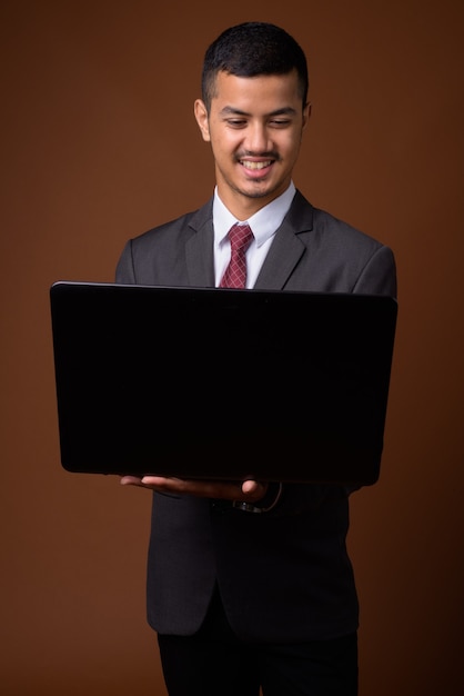 Young multi-ethnic Asian businessman against brown wall