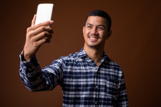 Young multi-ethnic Asian man against brown wall