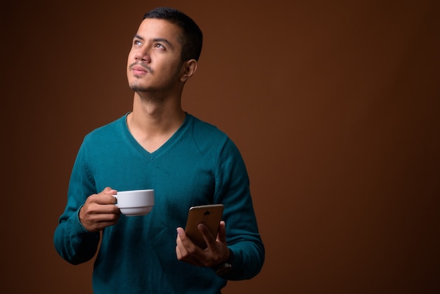 Young multi-ethnic Asian man against brown wall