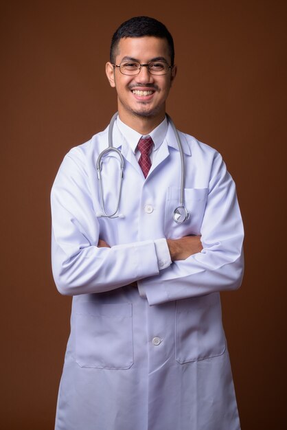 Young multi-ethnic Asian man doctor against brown wall