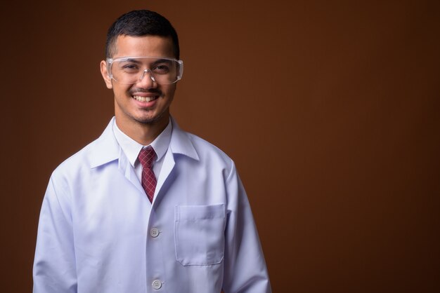 Young multi-ethnic Asian man doctor against brown wall