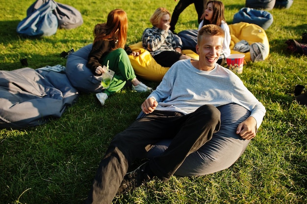 Young multi ethnic group of people watching movie at poof in open air cinema Close up portrait of funny guy