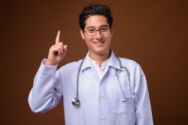 Young multi-ethnic handsome man doctor against brown background