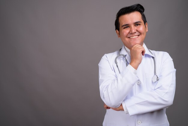 Young multi-ethnic man doctor against gray wall