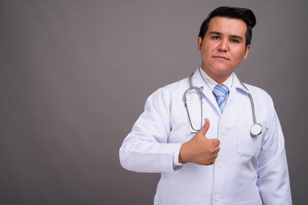 Young multi-ethnic man doctor against gray wall