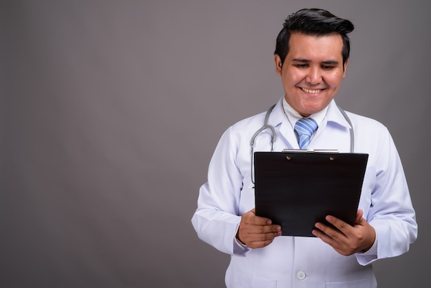 Young multi-ethnic man doctor against gray wall