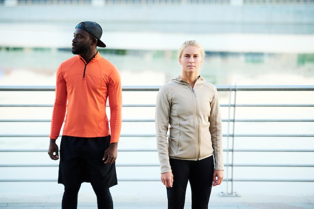 Young multicultural runners or athletes in activewear standing against riverside