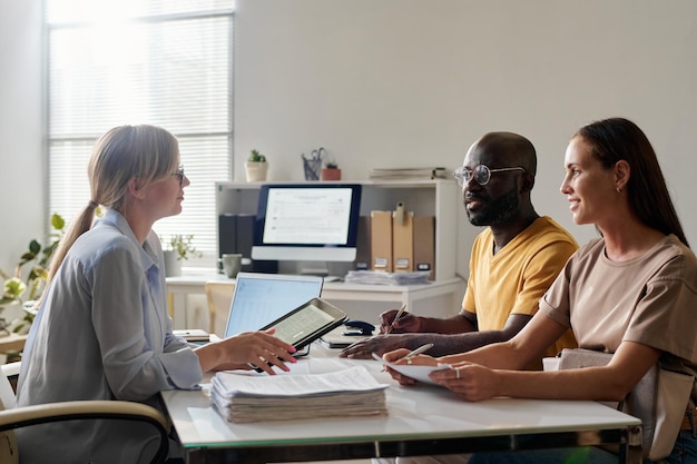 Young multiethnic couple having consultation with lawyer while sitting at table in office