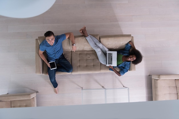 Young multiethnic couple relaxes in the luxury living room, using a tablet and laptop computer top view