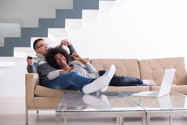 Young multiethnic couple relaxing on the sofa in the luxury living room, using a laptop and remote control