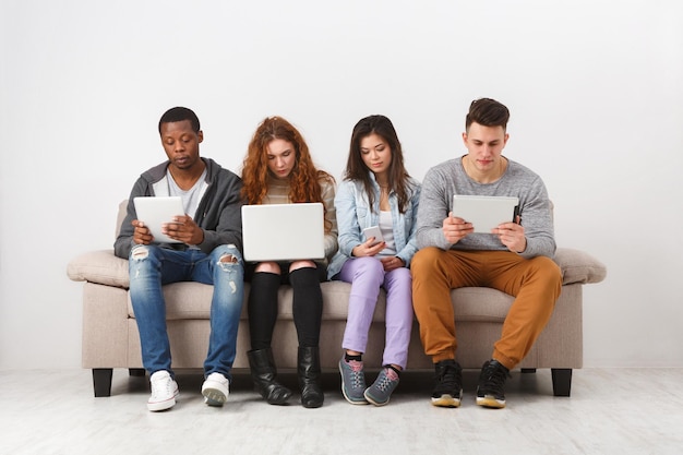 Photo young multiethnic people with gadgets, addiction concept. friends sitting on sofa indoors and working on project