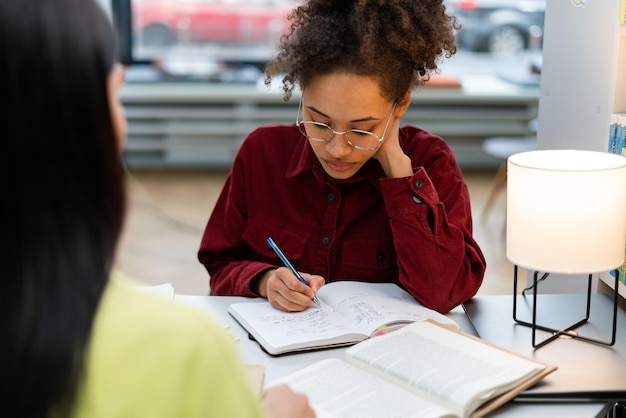 Young multiethnic women studying together at library High school or college students studying and reading together in library