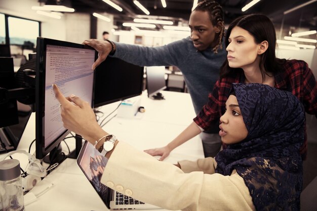 young multiethnics business team of software developers working together using laptop computer while writing programming code at modern startup office