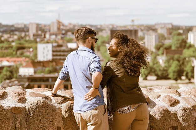 Young multiracial couple looking at each other with city skyline on the background as diversity friendship and togetherness travel concept. Vilnius, Lithuania