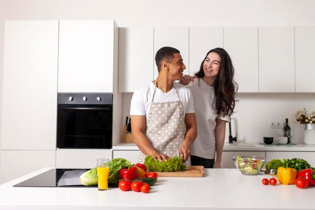 Young multiracial couple prepares veggie salad in white modern kitchen