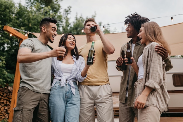 Young multiracial people drinking beer on camping trip chatting joking and laughing together