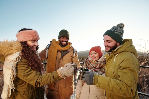 Young multiracial people in winterwear clinking with mugs of hot drinks