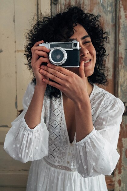 Young multiracial woman holding vintage camera taking a picture looking at camera VerticalTourism