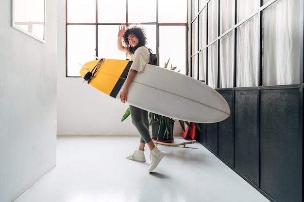 Young multiracial woman leaves the apartment carrying a surf\
board to go surfing in the beach sports concept lifestyle\
concept