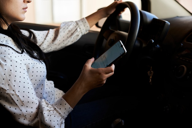 若い多民族の女性のテキストメッセージと車の運転車の運転中に携帯電話を使用している女性