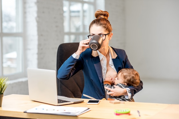 Фото Молодой многозадачный бизнесмен кормит своего маленького сына грудью во время перерыва, попивая кофе в офисе