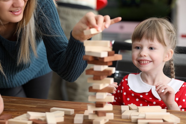 Young mum with little daughter play game in wood block