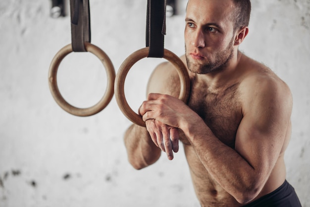 Young muscular attractive man naked torso posing against gymnastics rings