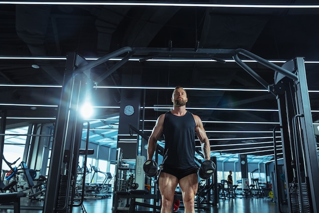 Giovane atleta caucasico muscolare che si allena in palestra, facendo esercizi di forza