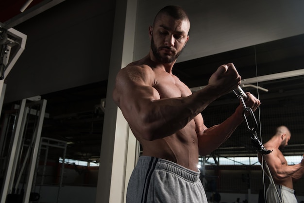 Young Muscular Fitness Bodybuilder Doing Heavy Weight Exercise For Biceps On Machine With Cable In The Gym