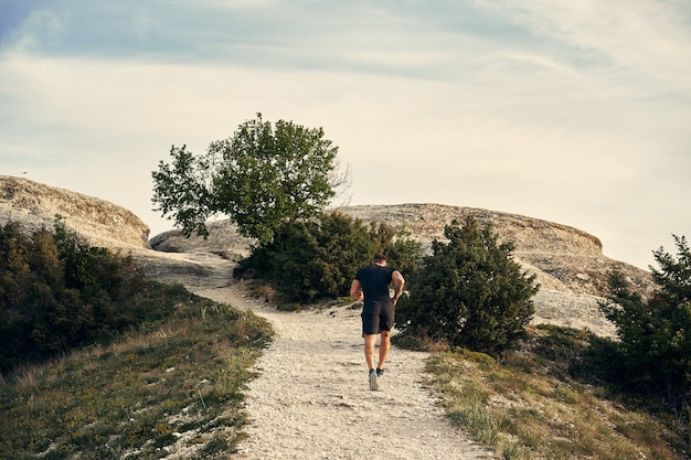 Young muscular male athlete running up the hill