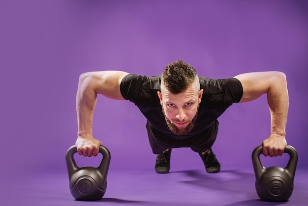 Young muscular man doing exercises with weight on purple studio background. copy space