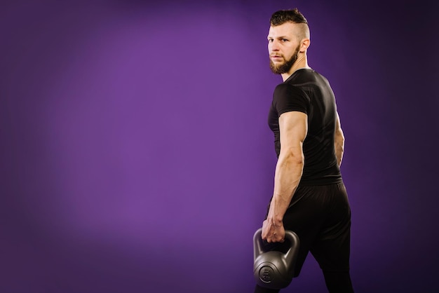 보라색 스튜디오 배경에서 무게로 운동을 하는 젊은 근육질의 남자. 복사 공간