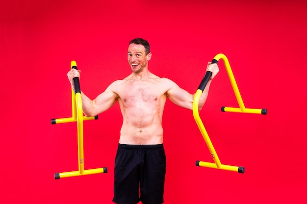 Young muscular man doing parallel bar exercises in a dark white red studio with copy space